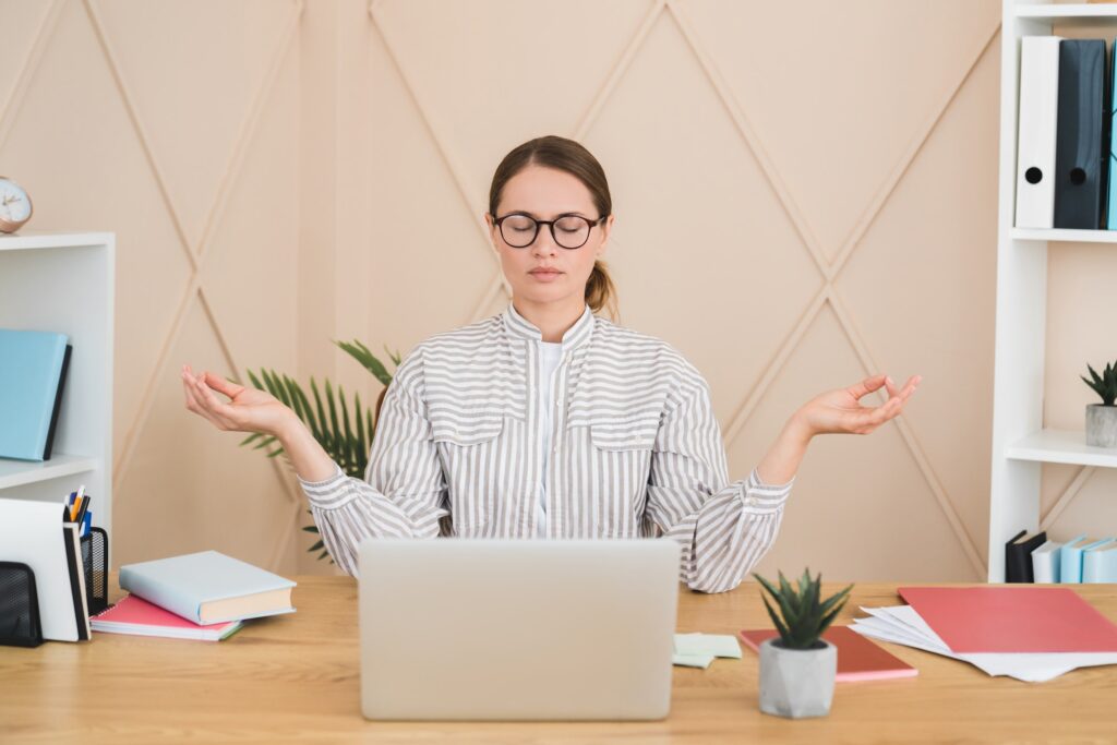 Businesswoman meditating yoga practice on workplace after hard day, deadline concept. Stress relief