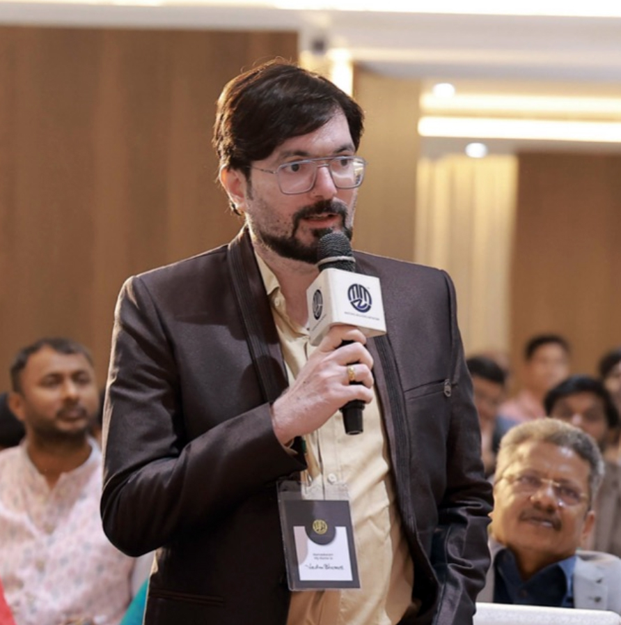 A professional picture of Vedam Bharath Suman, smiling warmly, wearing a crisp, white shirt and a dark blazer.