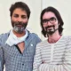 "Two men standing side-by-side on a movie set. On the left is the user, wearing a black and white checked shirt, and on the right is director Trivikram Srinivas, wearing a white and grey striped shirt and glasses."